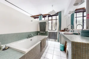 Vaste salle de bain lumineuse avec deux vasques, carrelage mosaïque et fenêtre atelier.