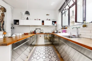Cuisine équipée en U, meubles en inox, carreaux métro blancs et verrière atelier.