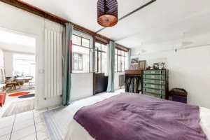 Chambre lumineuse avec grandes fenêtres sur cour, rideaux colorés et rangements intégrés.