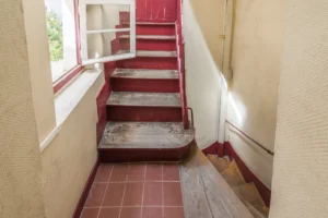 Parties communes anciennes avec escalier bois et carrelage d’époque, immeuble parisien typique