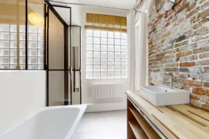 Salle de bain avec verrière et mur en brique dans un local atypique du 11ᵉ arrondissement parisien.