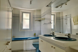 Salle de bain avec baignoire, double vasque et lumière naturelle dans un appartement à Paris 16, à rénover.