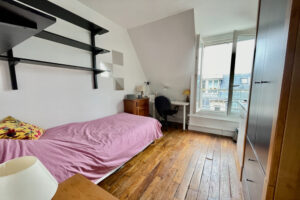 Chambre de service lumineuse avec parquet ancien et coin bureau dans un immeuble à Paris 16.