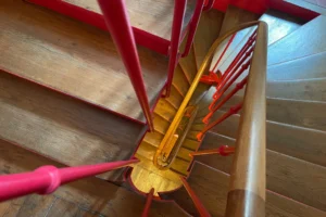 Escalier ancien en bois avec rampe rouge, cage d’escalier typique du charme parisien.