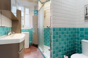 Salle d’eau fonctionnelle avec douche vitrée, meuble vasque et WC dans un décor coloré.