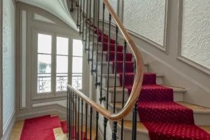 Montée d’escalier élégante dans immeuble ancien typique du 9ᵉ, moulures murales et rampe en bois massif.