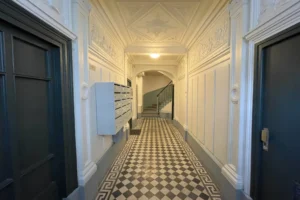 Entrée de l’immeuble avec moulures d’époque, carreaux de ciment noirs et blancs, et boîtes aux lettres intégrées.