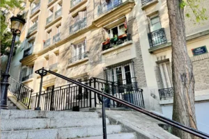 Accès privatif avec grille noire, porte d'entrée et pavés parisiens.