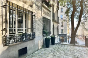 Façade de l’immeuble en briques avec grille en fer forgé et vue sur la rue Chappe, Paris 18ᵉ, quartier du Sacré-Cœur.