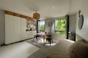 Salon baigné de lumière avec vue sur la verdure, dans un appartement à vendre à Paris 19, quartier Belleville.