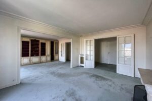 Séjour avec moulures anciennes, portes vitrées et bibliothèque murale dans un appartement à Paris 16.