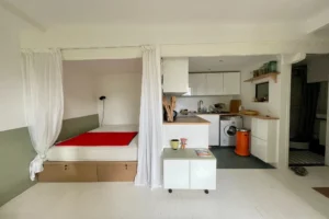 Coin nuit optimisé avec rideaux et cuisine ouverte équipée dans un appartement à Paris 19, quartier Belleville.