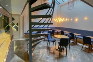 Vue de la salle du local commercial restaurant à Paris 10 avec escalier hélicoïdal et banquettes sous verrière