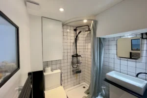 Salle d’eau rénovée avec douche à l’italienne, carrelage métro et robinetterie noire dans un appartement à Paris 19, quartier Belleville.