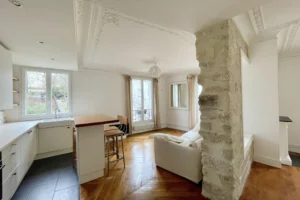 Salon lumineux avec cuisine ouverte, parquet en point de Hongrie et murs en pierre apparente à Montmartre, Paris 18ᵉ.