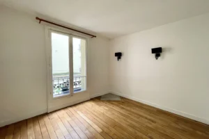 Chambre avec parquet bois et fenêtre donnant sur cour intérieure.