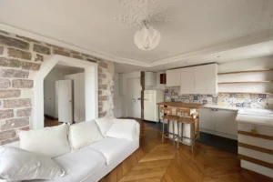Séjour avec cuisine ouverte, carreaux de ciment colorés, parquet en point de Hongrie et murs en brique dans un appartement à Montmartre, Paris 18ᵉ.