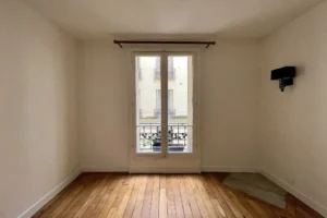 Pièce avec parquet ancien, appliques murales et fenêtre, idéale pour bureau ou coin nuit.