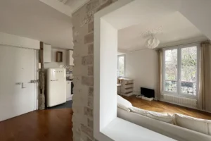 Entrée de l’appartement avec vue sur le séjour lumineux, la cuisine ouverte et les fenêtres donnant sur les Arènes de Montmartre, Paris 18ᵉ.