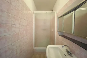 Salle de bains avec carrelage mural, miroir, lavabo et radiateur sèche-serviette.
