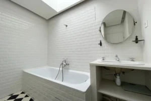 Salle de bain avec baignoire, carrelage métro blanc et miroir rond, dans un appartement à Montmartre, Paris 18ᵉ.
