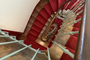 Escalier ancien en bois avec moquette rouge et rampe en fer forgé dans un immeuble haussmannien à Montmartre, Paris 18ᵉ.