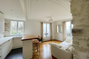 Cuisine ouverte et salon lumineux avec parquet ancien et mur en pierre apparente dans un appartement à Montmartre, Paris 18ᵉ.