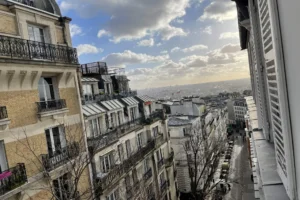 Vue dégagée sur les toits parisiens et une rue pittoresque de Montmartre depuis un appartement à vendre dans le 18ᵉ arrondissement.