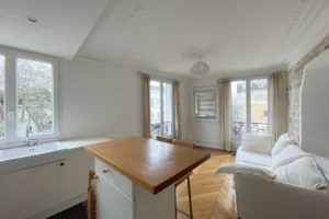 Petit salon chaleureux avec parquet ancien, moulures au plafond et mur en briques, typique de l'immobilier haussmannien à Paris 18ᵉ, quartier des Abbesses.