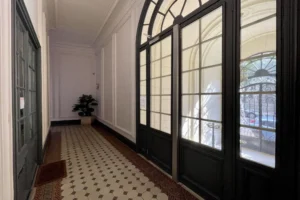 Entrée élégante d’un immeuble haussmannien à Paris 18e avec portes vitrées, grille en fer forgé et sol en carreaux de ciment d’origine.