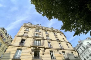 Façade en pierre de taille d’un immeuble haussmannien à Paris 18e, donnant sur la place Charles Dullin, avec ciel bleu et feuillage en perspective.
