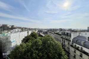 Vue lumineuse sur les toits parisiens et la végétation de Montmartre, dans le 18e arrondissement de Paris, sous un ciel ensoleillé.