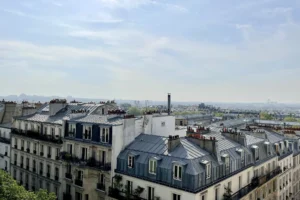 Vue dégagée sur les toits typiques parisiens depuis un appartement situé à Montmartre, Paris 18e, avec horizon urbain en arrière-plan.