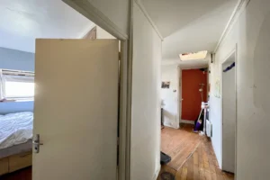 Vue sur le couloir d’un appartement à Montmartre, Paris 18e, desservant une chambre, une pièce de vie et des rangements sous les toits.