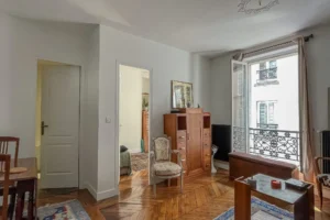 Salon lumineux avec parquet en point de Hongrie, grande fenêtre et mobilier ancien, situé dans un appartement à vendre à Paris 10ᵉ, quartier Faubourg Saint-Denis.