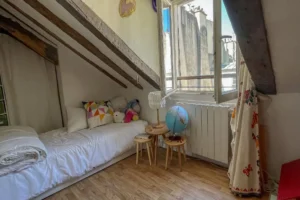Petite chambre mansardée avec lit d'enfant et vue sur les toits du Faubourg Saint-Denis.