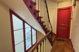 Escalier ancien avec rampe en bois, parquet en point de Hongrie et fenêtres sur cour, dans un immeuble à Paris 10ᵉ, quartier Faubourg Saint-Denis.