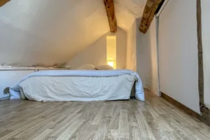 Chambre sous combles avec lit double, éclairage tamisé et poutres apparentes.