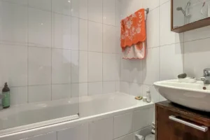 Salle de bains avec baignoire et vasque, murs en faïence blanche, dans un appartement à vendre à Paris 10ᵉ, quartier Faubourg Saint-Denis.