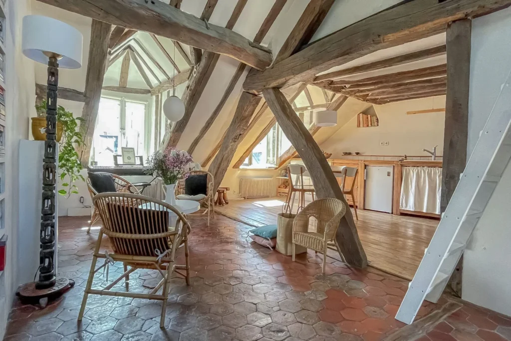 Grand salon sous combles avec espace cuisine ouvert et sol en tomettes anciennes.
