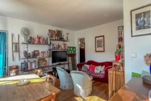 Salon avec bibliothèque murale sur mesure, canapé et fauteuils, parquet ancien et mobilier en bois, offrant un espace de vie chaleureux et fonctionnel dans un appartement situé rue du Faubourg Saint-Denis, secteur Gare du Nord à Paris 10.