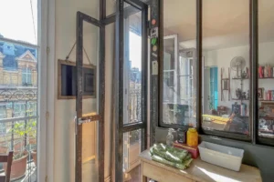 Verrière de style atelier séparant la cuisine de la pièce de vie, avec portes vitrées ouvrant sur le balcon filant et apportant une belle luminosité naturelle, appartement situé rue du Faubourg Saint-Denis, secteur Gare du Nord à Paris 10.