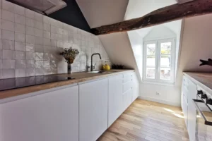 Crédence blanche et placards modernes dans une cuisine équipée avec finitions bois clair.