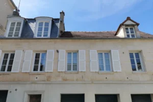 Façade d’un immeuble ancien situé en plein centre-ville de Chantilly, avec volets blancs et fenêtres symétriques.