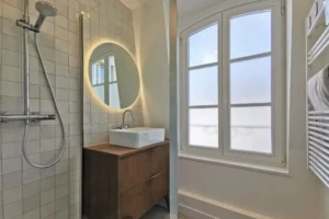 Salle de bains moderne avec douche à l’italienne, meuble vasque suspendu et fenêtre.