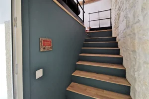 Escalier en bois avec mur en pierre naturelle, menant à la pièce de vie principale.