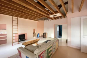 Vue sur salon avec cheminée et échelle menant à une mezzanine, ambiance chaleureuse sous plafond cathédrale en bois.