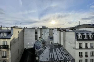 Vue depuis l’appartement sur les toits de Paris au coucher du soleil, lumière traversante et dégagement.