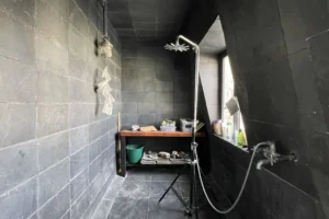 Douche à l’italienne avec murs noirs et rangement en bois sous la fenêtre.