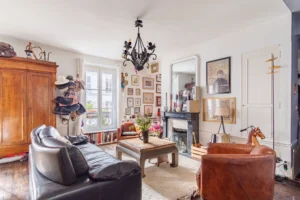 Salon chaleureux avec cheminée, parquet ancien et grande fenêtre dans un appartement à vendre Paris 18 Montmartre